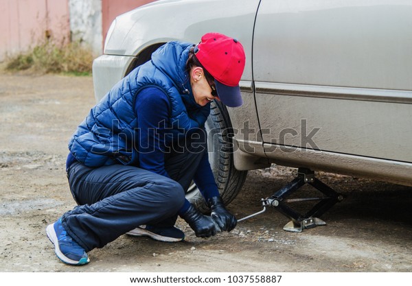 Seasonal change of tires. Young positive woman alone\
change a tire on the\
car