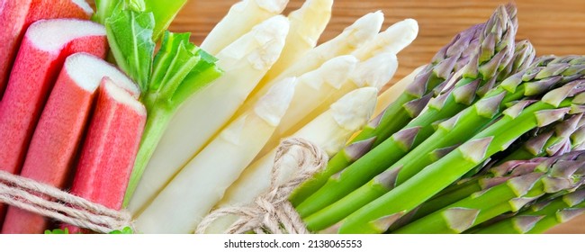 Seasonal fresh green and white asparagus with rhubarb on wooden background closeup
