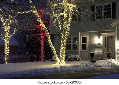 Seasonal House Outdoors Decoration. Background With House Front Yard, Covered By Fresh Snow Decorated For Christmas And New Year Holidays. Night Scene.