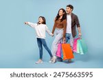 Seasonal sales. Family holding colorful paper shopper bags, girl pointing aside at free space, standing on blue background