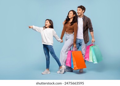 Seasonal sales. Family holding colorful paper shopper bags, girl pointing aside at free space, standing on blue background - Powered by Shutterstock