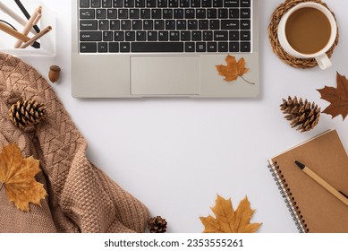 Seasonal workspace infusion. Overhead view: laptop, stationery stand, knitted plaid, hot cocoa, spiral organizer, pen, pine cones, maple leaves. Welcome autumn into your work setup - Powered by Shutterstock