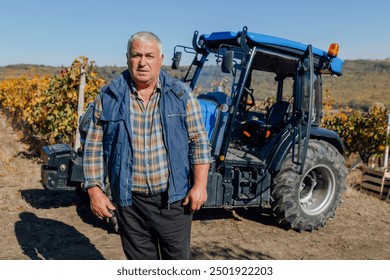 A seasoned farmer, bathed in sunlight, stands proudly beside a trusty tractor in the heart of a flourishing vineyard. - Powered by Shutterstock