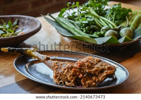 Seasoned fried chicken served on stainless steel plate with raw vegetables and chili sauce on wooden table