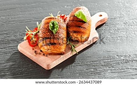 Seasoned pieces of grilled meat placed on a kitchen table surrounded by fresh ingredients, vegetables and herbs. Healthy eating, home cooking, food blogs and conscious food preparation concept.