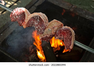 Seasoned Raw Rump Steak On The Grill With Fire, The Traditional Churrasco Gaúcho, Brazilian Barbecue Made Outdoors.