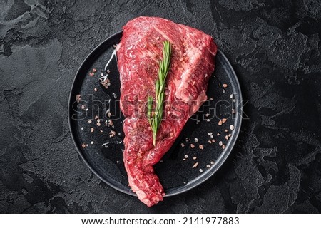 Seasoned raw tri-tip beef meat steak on plate. Black background. Top view.