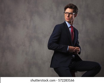 Seated Business Man Buttoning His Suit And Looks Over His Shoulder In Studio, Sitting On A Stool