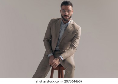 Seated Cool Businessman Holding The Chair And Wearing Eyeglasses In A Fashion Pose
