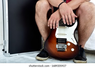 Seated Man Holding Guitar Between His Legs With Hard Case Beside