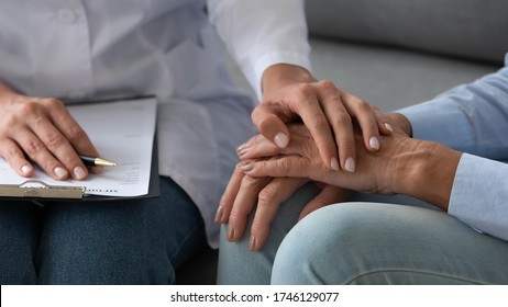 Seated on couch social service homecare nurse worker in white coat supports old patient hold hand encourages her close up, cancer diagnose, overcome illness, psychological help express empathy concept - Shutterstock ID 1746129077