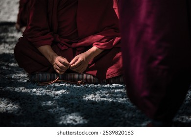 Seated person in maroon robes meditates with hands clasped, holding prayer beads on a textured surface. - Powered by Shutterstock