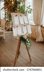 Seating plan, wooden board on an easel, paper cards with table numbers, a composition of flowers and tropical leaves, raspberry branches.