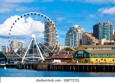 Seattle ferris wheel, waterfront and skyline on a bright sunny day with blue sky and clouds.  View is from the water.  Close up