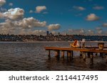 SEATTLE SKYLINE FROM MERCER ISLAND WITH THE 1-90 FLOATING BRIDGE AND WHITE PUFFY CLOUDS AND A BOAT DOCK WITH A BRIGHT YELLOW CHAIR AND POST