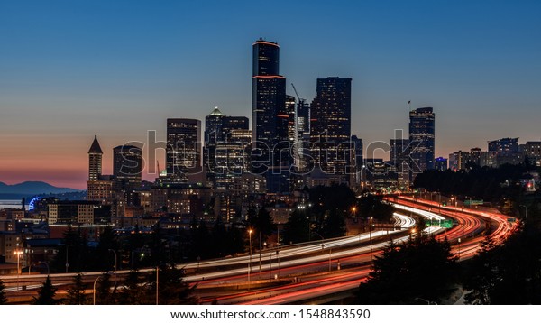 Seattle skyline, at\
sunset. The cars along the highway are creating light trails, due\
to a slow shutter speed
