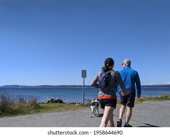 Seattle, WA USA - circa April 2021: View of a man and woman walking their dog along the beach trail at Discovery Park on a cloudless day.