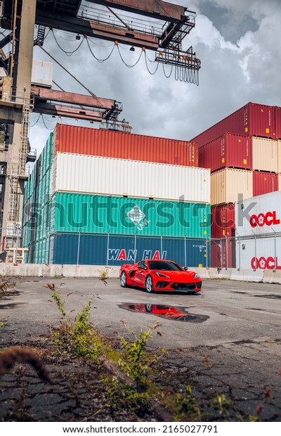Seattle, WA,\
USA\
June 4, 2022\
Red Corvette C8 Stingray parked on asphalt with\
shipping containers in the\
background