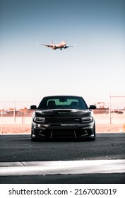 Seattle, WA, USA
March 2, 2022
Dodge Challenger Hellcat SRT In Black Parked With A Plane Coming In For A Landing The Background