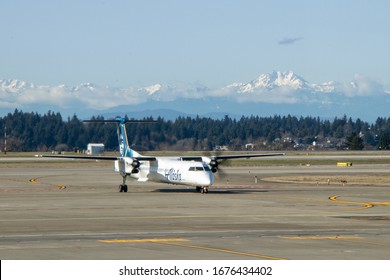 Seattle, Washington/ USA - February 18, 2020: An Alaska Airlines (Horizon Air) turboprop taxis near Runway 34R at Seattle-Tacoma International Airport, with the Olympic Mountains in the distance