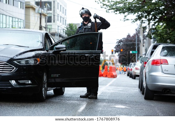 Seattle, Washington / USA - July 1 2020:\
Seattle Police removing his riot baton while entering a squad car,\
in the Capitol Hill Occupation Protest\
(CHOP)