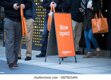 SEATTLE, WASHINGTON/USA - January 22, 2018: Now Open Sign Outside Of The Amazon Go Store At The Downtown Seattle Headquarters, With Shoppers Holding Orange Reusable Bags In The Background