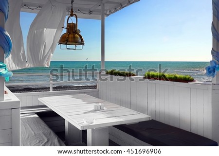 Seaview Restaurant Interior. White Terrace Or Veranda With Separated Cabins Under Tent And White Curtains. Wooden Furniture.  Hanging Lanterns.