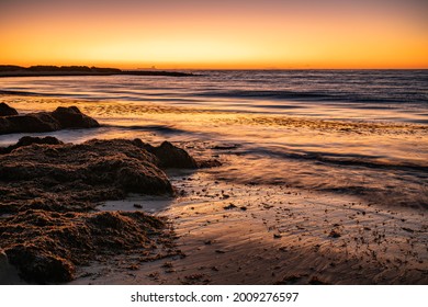 Seaweed Wrack Onshore At Pages Beach Geraldton Western Australia. Sunset, Long Exposure Showing The Movement Of The Waves And Of The Water. Container Ship Silhouetted On The Horizon.