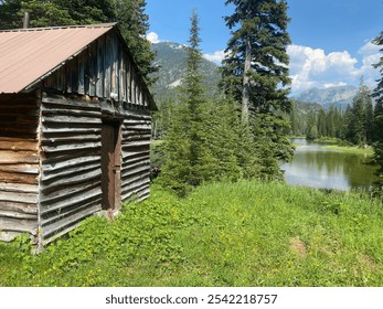 Secluded wood hunting cabin in green mountain valley surround by a lake and evergreen trees - Powered by Shutterstock