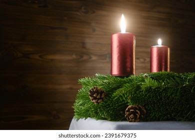 For the second Advent, two burning candles on an Advent wreath against a wooden background