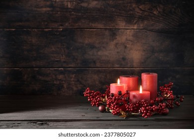 Second Advent with two lit red candles in a wreath from berries with Christmas decoration against a dark rustic wooden background, copy space, selected focus, narrow depth of field