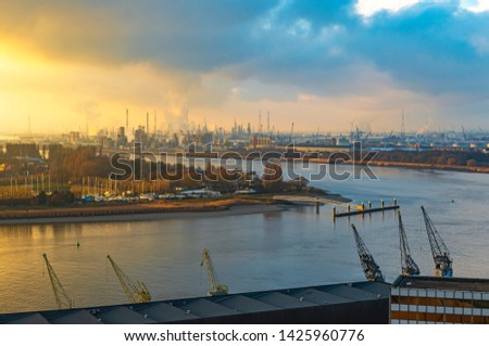 The second largest industrial harbor of Europe at sunset with cranes in the foreground, chemical and nuclear plants in the background and the Scheldt River, Antwerp, Belgium.