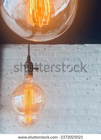 Second round light bulb in its row hanging from the ceiling with blank space of white brick wall for text or quotes portray idea, design thinking, thought, clever, smart, philosophy, light, learning.
