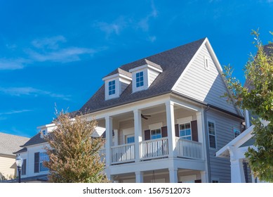 Second story porch with white painted outer edge and banister. Dormer roof windows with weathered shingle siding tiles under cloud blue sky. Country –style houses in suburbs Dallas, Texas, USA