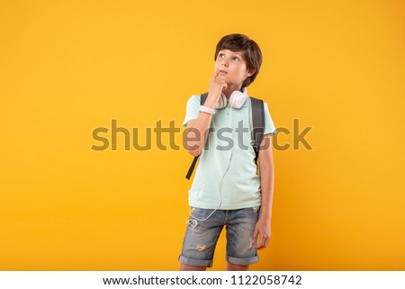 Second thoughts. Serious dark-haired boy wearing headphones and a schoolbag and thinking