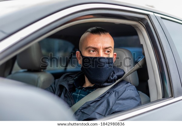 second wave coronavirus man driving a car puts\
on a black mask during an epidemic, driver in a mask, protection\
from the virus. Driver in black car. , disease, infection,\
quarantine, covid-19