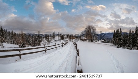 Secondary countryside alpine road in remote mountain village, snow drifts and wood fence on wayside