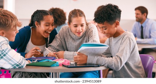 Secondary Or High School Students Collaborating In Study Area With Teachers In Background - Powered by Shutterstock