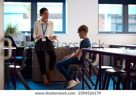 Secondary Or High School Teacher Sitting In Classroom With Unhappy Male Student After Lesson