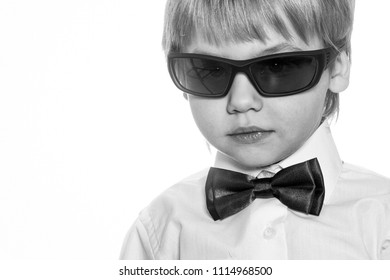 Secret Agent. The Dream Of A Child. Portarit Of Small Gentleman Special Agent Boy With Blonde Hair In White Shirt Red Formal Bow Tie And Sun Glasses Indoor On Light Background, Horizontal Picture
