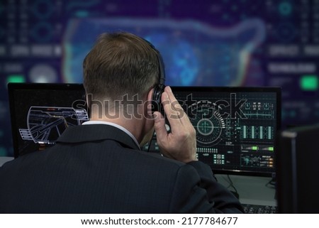 A secret agent wearing headphones watches the monitors and monitors in the military center. Concept: human surveillance, government official.