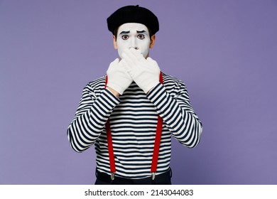 Secret embarrassed bewildered puzzled bemused sad young mime man with white face mask wears striped shirt beret cover mouth with hand isolated on plain pastel light violet background studio portrait