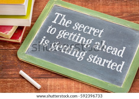 The secret to getting ahead is getting started - white chalk text on a slate blackboard with a stack of books against rustic wooden table