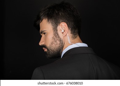 Secret Service Agent In Suit Using Earphone, Isolated On Black