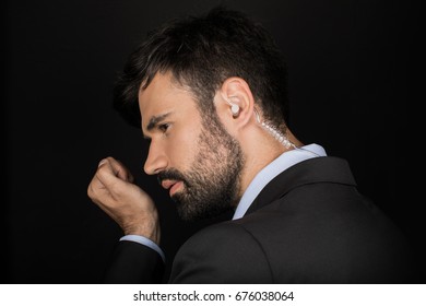 Secret Service Agent In Suit Using Earphone, Isolated On Black