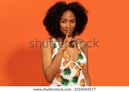 Secret summer trips sale. Playful attractive young african american woman in swimwear with pineapples holding finger on lips and looking at camera, isolated on orange background
