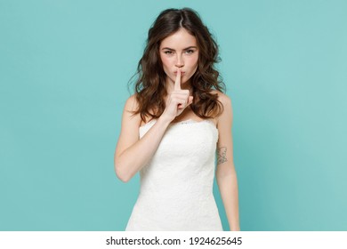 Secret tender bride young woman in white wedding dress saying hush be quiet with finger on lips shhh gesture isolated on blue turquoise background studio portrait. Ceremony celebration party concept