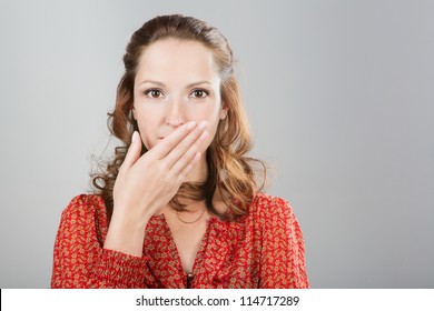 Secret Woman Saying Be Quiet. Girl With Hand In Front Of Mouth. Shut Up.In Red Blouse. Grey Background. Studio Shot.