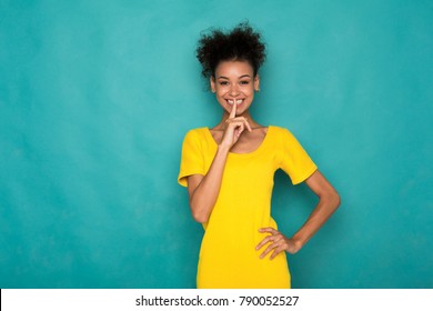 Secret. Young African-american Woman Put Finger On Lips, Hush Sign, Keep Silence. Happy Black Girl On Blue Studio Background