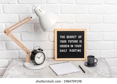 The secret of your future is hidden in your daily routine. Motivational quote on letter board, alarm clock, lamp on workplace. Concept inspirational quote of the day. Front view.